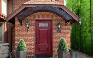 Home 32 Tinted polycarbonate entryway awning over an elegant front door, offering year-round rain and snow protection with a stylish architectural touch