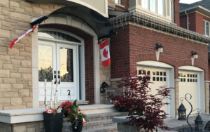 Home 31 Tinted polycarbonate awning installed over a front door of the canadian contemporary house' entrance with seasonal flags softly mounted on the brackets